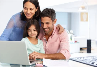 Smiling parents and young daughter gathered around a laptop at home, looking at the screen together.